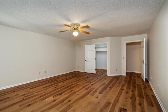 unfurnished bedroom with a walk in closet, a textured ceiling, ceiling fan, dark hardwood / wood-style floors, and a closet