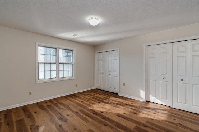 unfurnished bedroom featuring dark hardwood / wood-style floors, a textured ceiling, and two closets