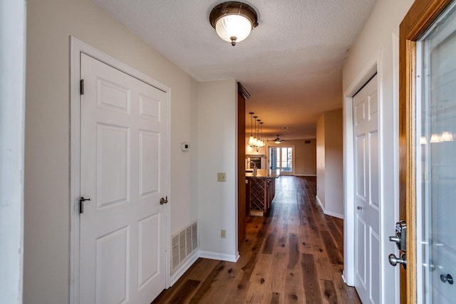 corridor with a textured ceiling and dark wood-type flooring