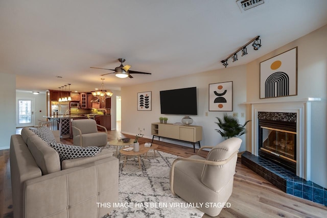 living room featuring ceiling fan with notable chandelier, wood-type flooring, and a tiled fireplace