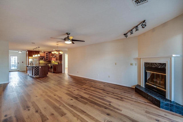 unfurnished living room with wood-type flooring, ceiling fan with notable chandelier, and track lighting