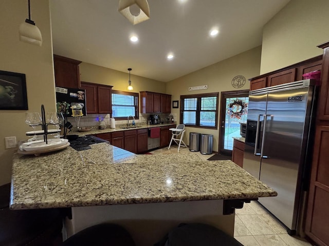 kitchen with kitchen peninsula, appliances with stainless steel finishes, tasteful backsplash, sink, and hanging light fixtures