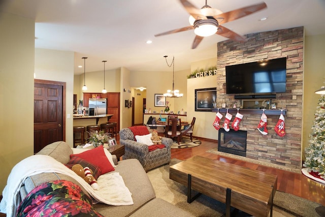 living room with hardwood / wood-style floors, ceiling fan with notable chandelier, a fireplace, and vaulted ceiling