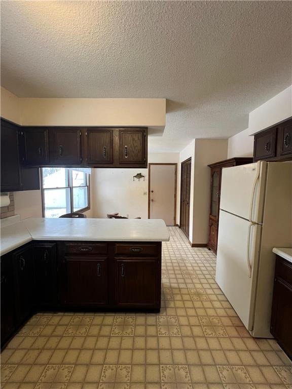 kitchen featuring dark brown cabinets, white refrigerator, kitchen peninsula, and a textured ceiling