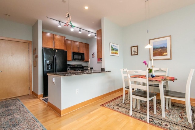 kitchen with light hardwood / wood-style flooring, kitchen peninsula, dark stone countertops, decorative light fixtures, and black appliances