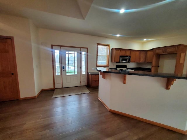 kitchen featuring a kitchen bar, kitchen peninsula, black stove, and dark hardwood / wood-style floors