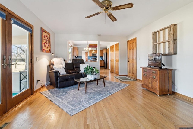 living room featuring ceiling fan with notable chandelier and light hardwood / wood-style floors