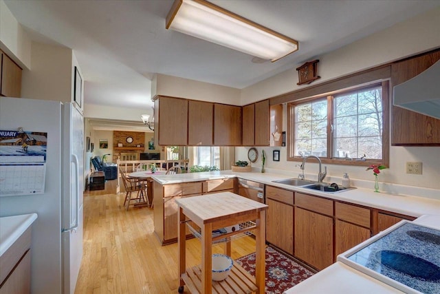 kitchen featuring sink, light hardwood / wood-style flooring, range hood, kitchen peninsula, and white fridge