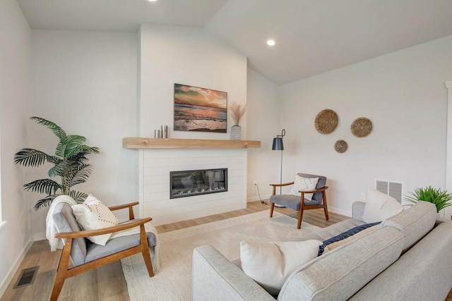 living room featuring lofted ceiling, light wood-style flooring, a glass covered fireplace, and visible vents