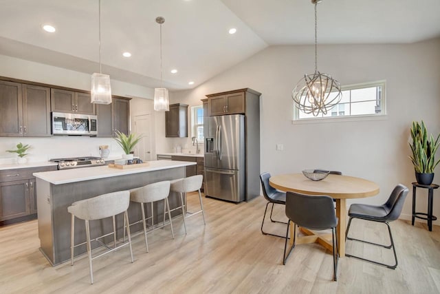 kitchen with vaulted ceiling, stainless steel appliances, decorative light fixtures, and light hardwood / wood-style floors