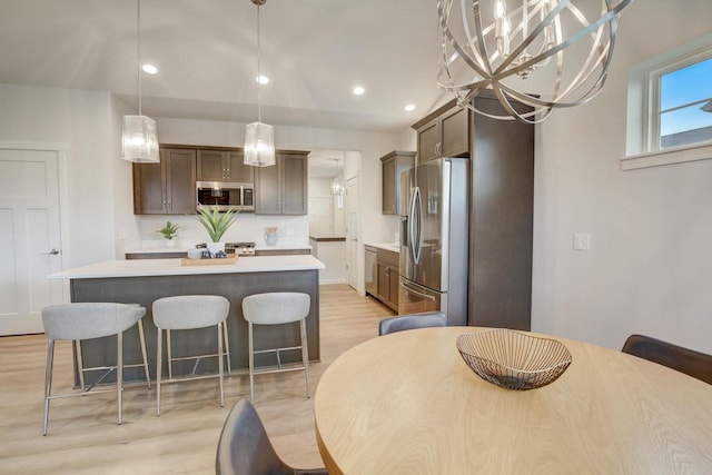 kitchen with an inviting chandelier, light hardwood / wood-style flooring, pendant lighting, a kitchen island, and appliances with stainless steel finishes