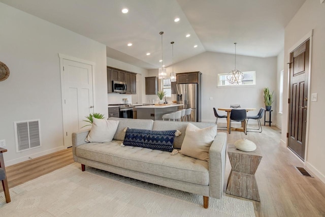 living room with a chandelier, light hardwood / wood-style flooring, and vaulted ceiling