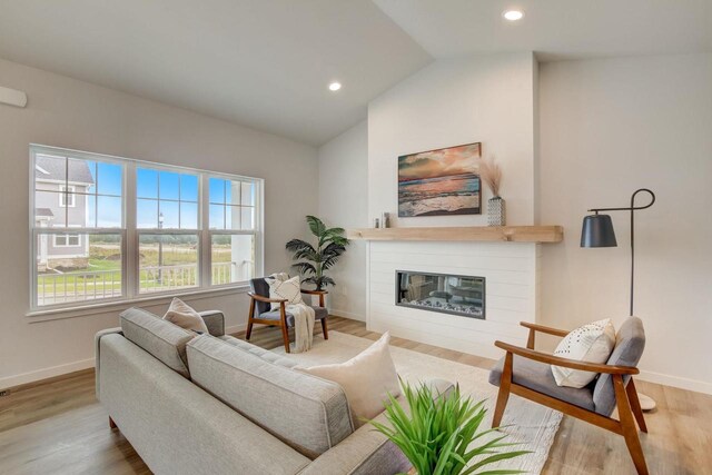 living room with a glass covered fireplace, vaulted ceiling, baseboards, and wood finished floors