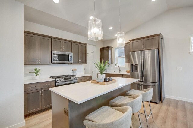 kitchen with a center island, stainless steel appliances, light countertops, a sink, and a kitchen breakfast bar