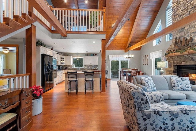 living room featuring high vaulted ceiling, ceiling fan with notable chandelier, light hardwood / wood-style flooring, a fireplace, and wood ceiling