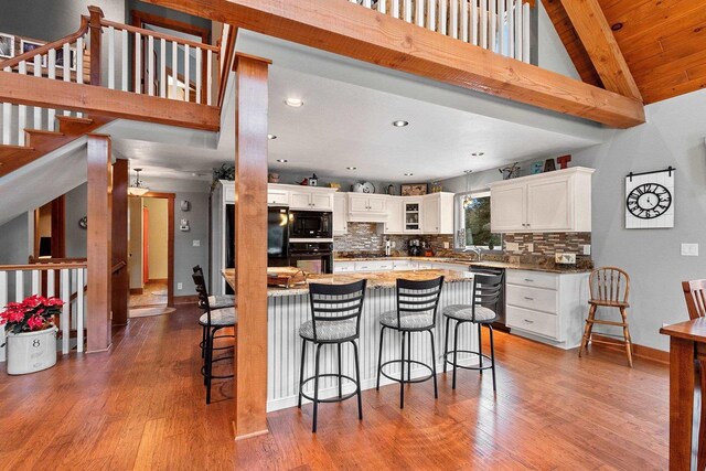 kitchen with decorative backsplash, black appliances, hardwood / wood-style flooring, vaulted ceiling with beams, and white cabinetry