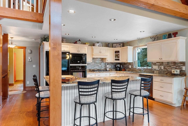 kitchen featuring a kitchen bar, hardwood / wood-style floors, light stone counters, and black appliances