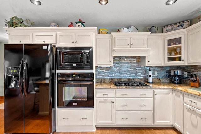 kitchen featuring black appliances, decorative backsplash, light stone countertops, light hardwood / wood-style floors, and white cabinetry