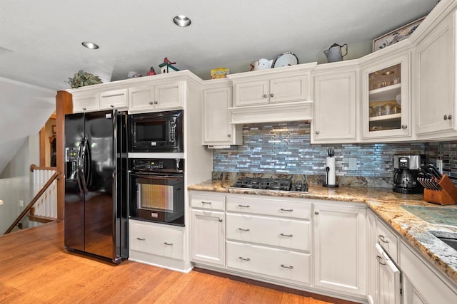 kitchen featuring white cabinetry, light stone countertops, light hardwood / wood-style flooring, backsplash, and black appliances