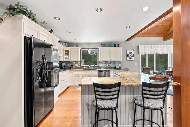 kitchen with light stone countertops, appliances with stainless steel finishes, backsplash, a kitchen breakfast bar, and white cabinetry