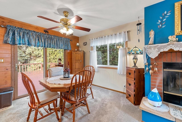 carpeted dining space featuring ceiling fan, wood walls, and a fireplace