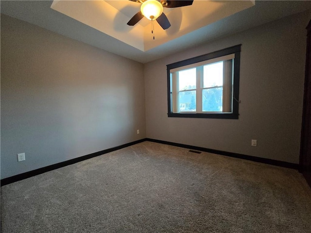 carpeted spare room featuring ceiling fan and a raised ceiling