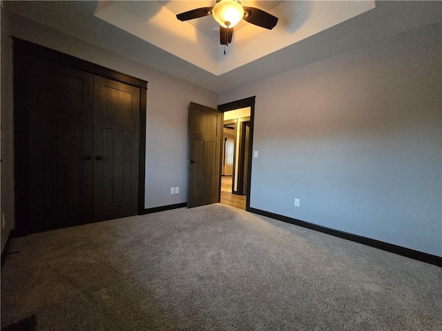 unfurnished bedroom with a tray ceiling, ceiling fan, a closet, and carpet floors