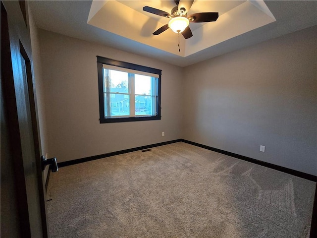 spare room with carpet, a tray ceiling, and ceiling fan