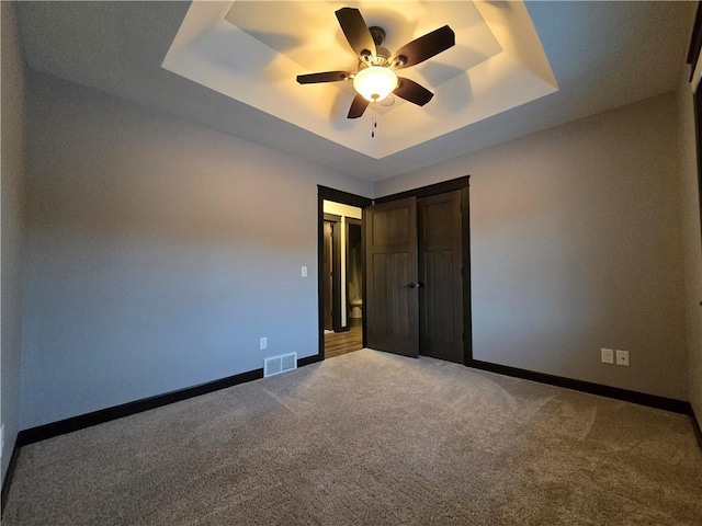 unfurnished bedroom featuring ceiling fan, a raised ceiling, and carpet floors