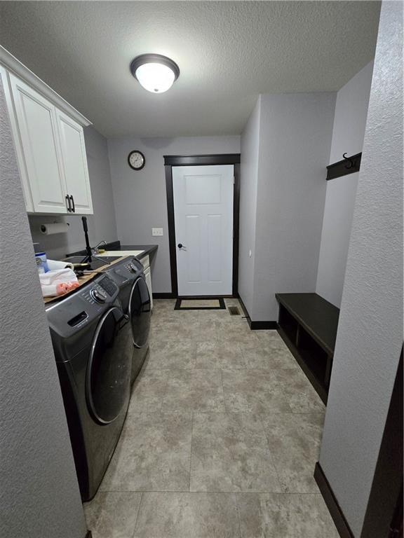 laundry room with cabinets, a textured ceiling, and washing machine and dryer