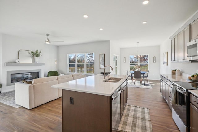 kitchen with a kitchen island with sink, sink, appliances with stainless steel finishes, and light hardwood / wood-style flooring