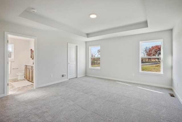 unfurnished bedroom featuring light carpet, connected bathroom, and a raised ceiling