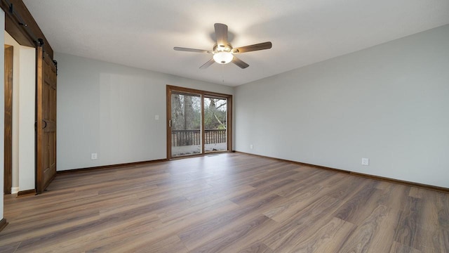 empty room featuring ceiling fan, a barn door, and wood-type flooring