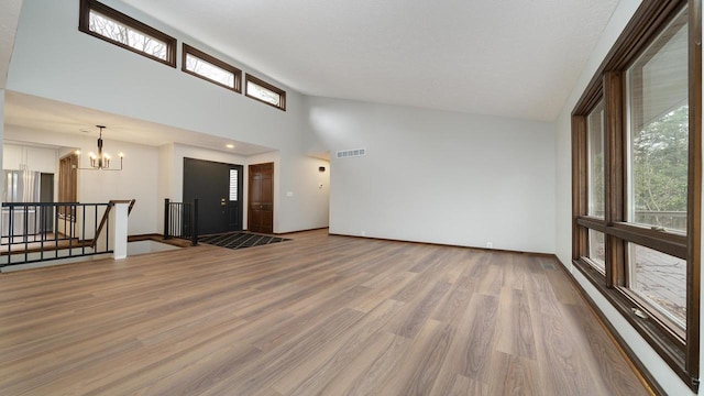 unfurnished living room featuring a textured ceiling, high vaulted ceiling, a notable chandelier, and light wood-type flooring