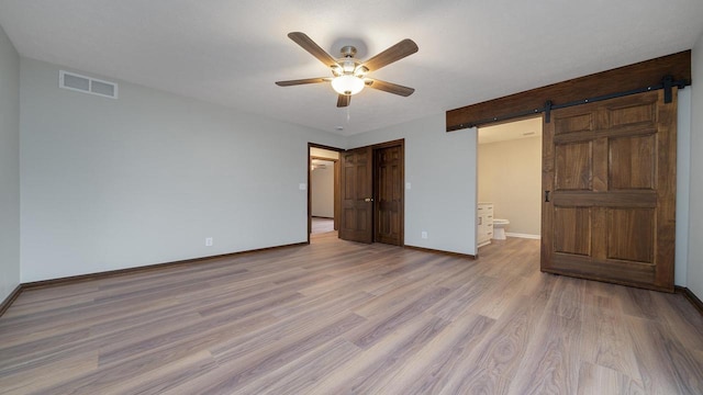 unfurnished bedroom featuring a barn door, ceiling fan, ensuite bathroom, and light hardwood / wood-style floors