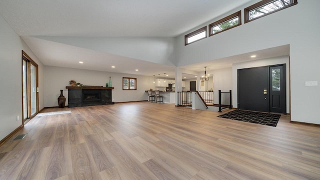 entryway with an inviting chandelier, high vaulted ceiling, and light hardwood / wood-style flooring