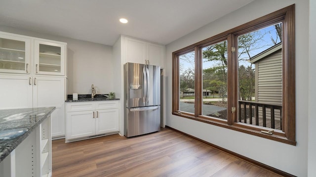 kitchen with stainless steel refrigerator with ice dispenser, light wood-type flooring, white cabinetry, and dark stone counters