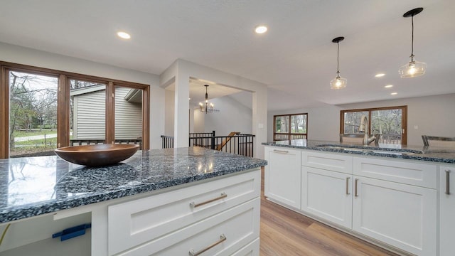 kitchen with dark stone counters, an inviting chandelier, sink, light wood-type flooring, and white cabinetry