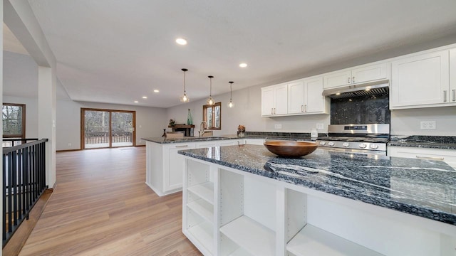 kitchen with dark stone counters, light hardwood / wood-style flooring, decorative light fixtures, white cabinetry, and stainless steel range with gas stovetop