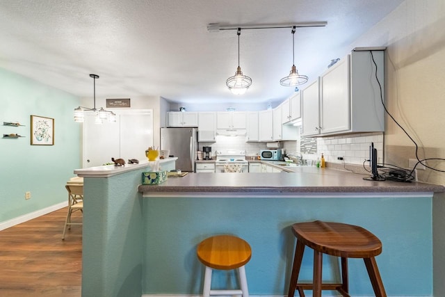 kitchen featuring white cabinetry, hanging light fixtures, stainless steel fridge, electric stove, and a breakfast bar