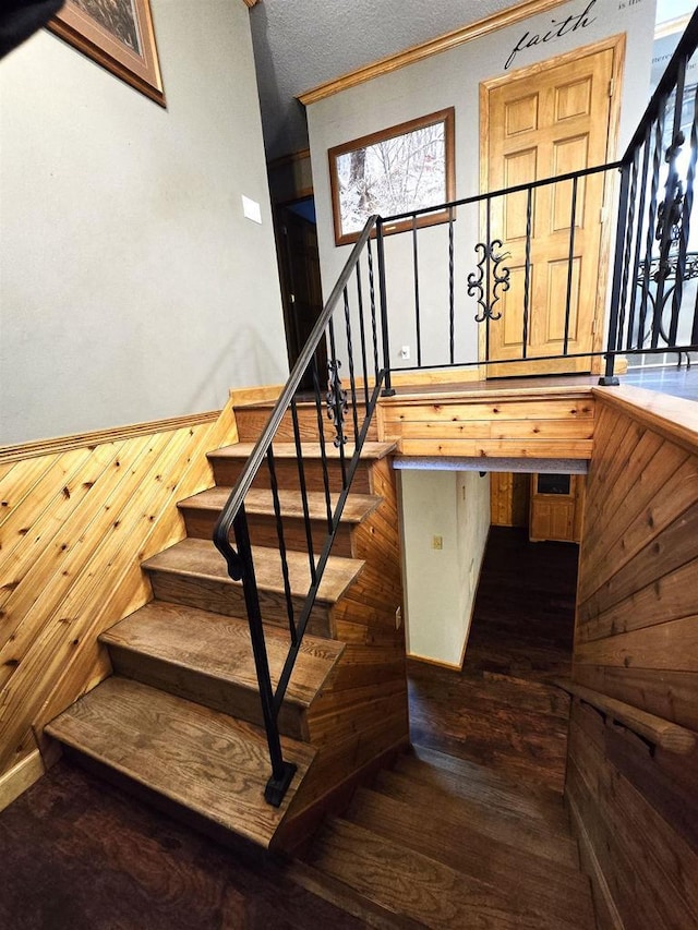 staircase with wooden walls, a textured ceiling, and hardwood / wood-style flooring