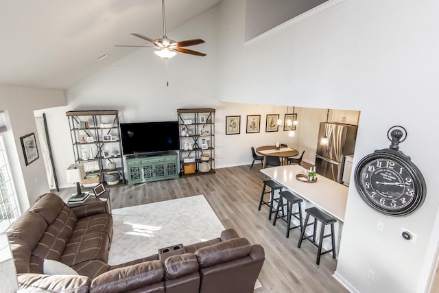 living room featuring ceiling fan with notable chandelier, light wood-type flooring, and high vaulted ceiling