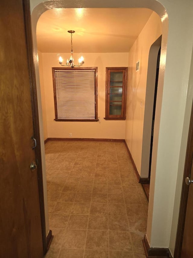 hallway featuring dark tile patterned flooring and a notable chandelier