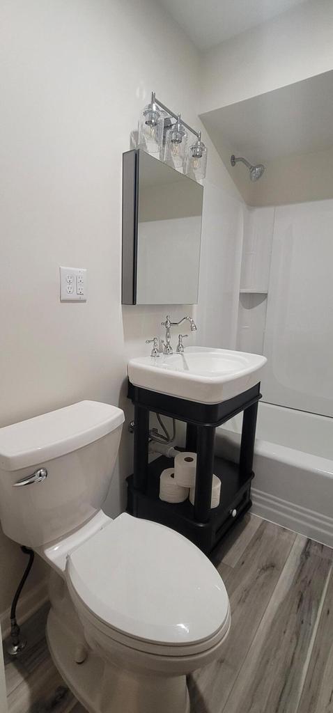 full bathroom with bathing tub / shower combination, sink, hardwood / wood-style floors, and toilet