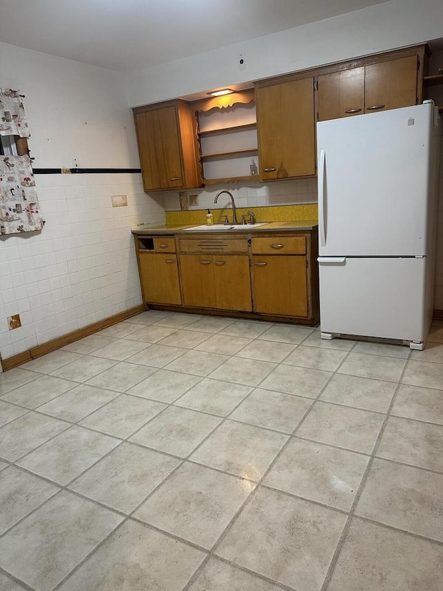 kitchen with white refrigerator, light tile patterned flooring, sink, and tile walls