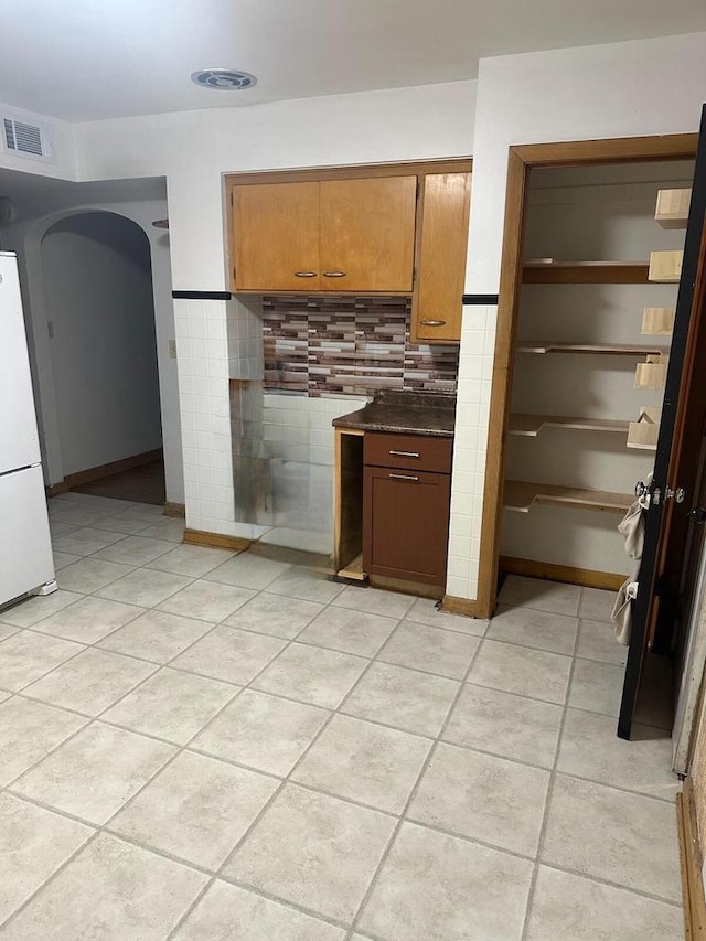 kitchen with white fridge, light tile patterned flooring, and backsplash