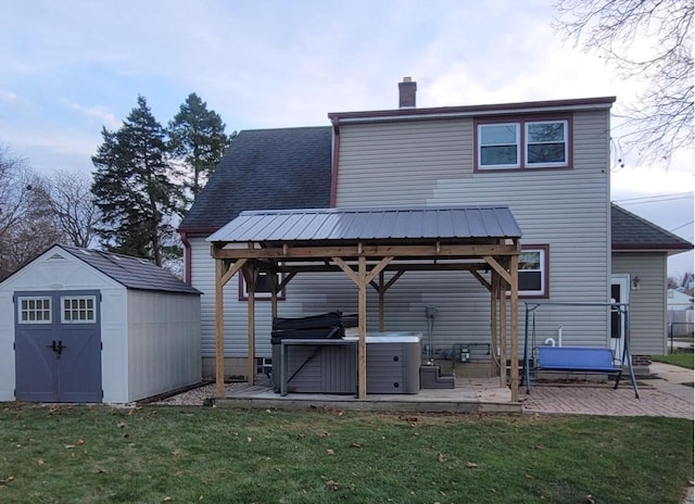 back of house featuring a patio, a hot tub, a storage unit, and a lawn