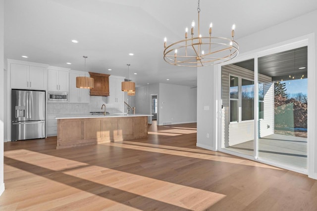 kitchen featuring pendant lighting, white cabinets, a spacious island, appliances with stainless steel finishes, and light hardwood / wood-style floors