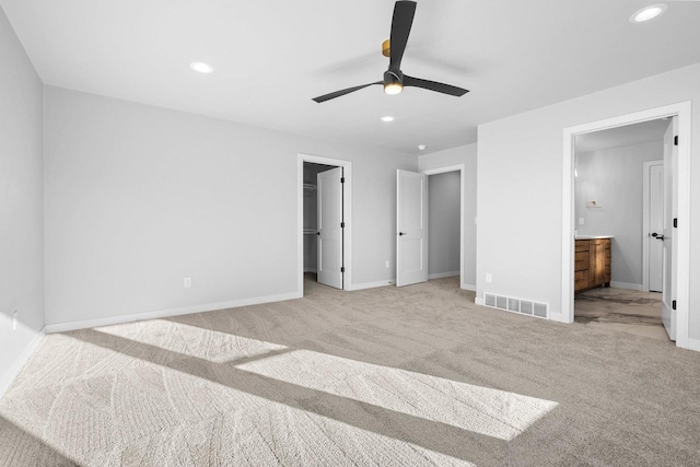 unfurnished bedroom featuring light carpet, a walk in closet, ensuite bath, ceiling fan, and a closet