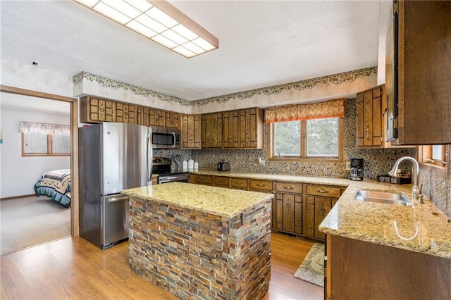 kitchen with light stone counters, stainless steel appliances, sink, light hardwood / wood-style flooring, and a kitchen island